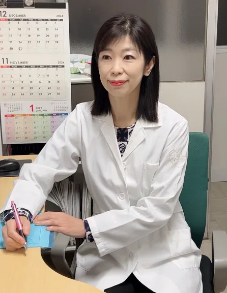 白衣姿で机に座りペンを持つ木村容子先生