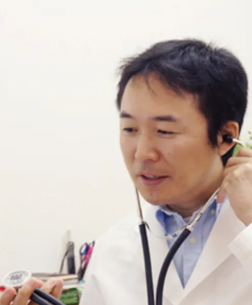 白衣姿で聴診器を耳に当てる來村昌紀先生